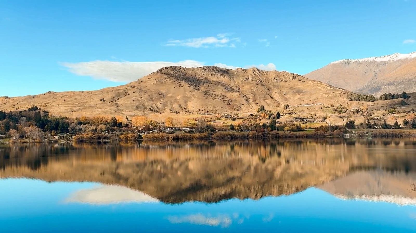 Golden hills and blue sky reflected in a still Queenstown lake