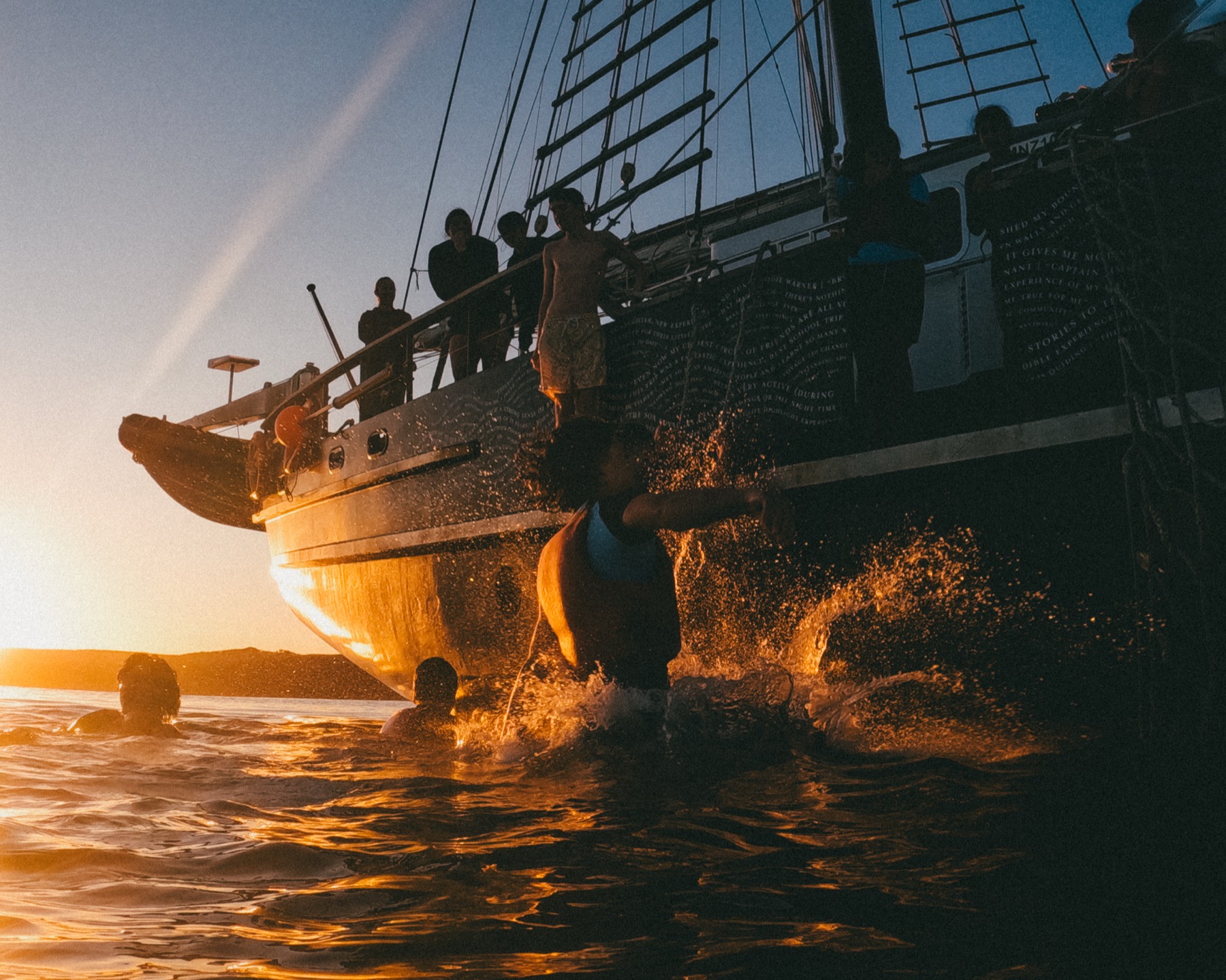 Trainees swimming beside the ship at sunset